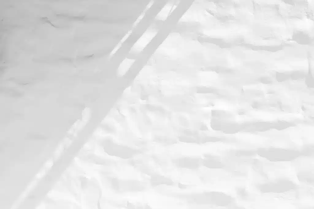 Texture de mur blanc rustique et brut éclairée par le soleil, avec une forte ombre portée oblique créant un motif minimaliste.