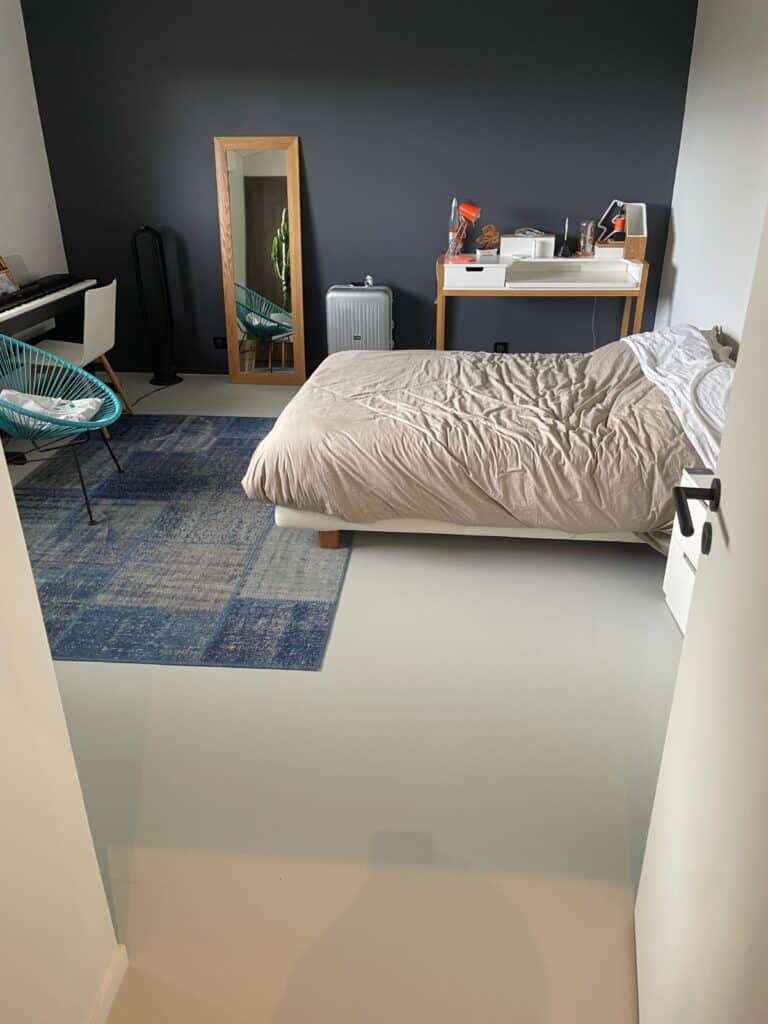 Chambre moderne minimaliste : mur bleu marine et lit design. Chambre moderne : mur accent bleu marine, lit beige, bureau, tapis patchwork bleu et chaise Acapulco turquoise.